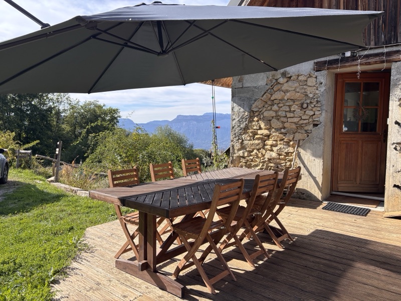 La terrasse du gîte, grande table en bois sous le parasol, face aux montagnes